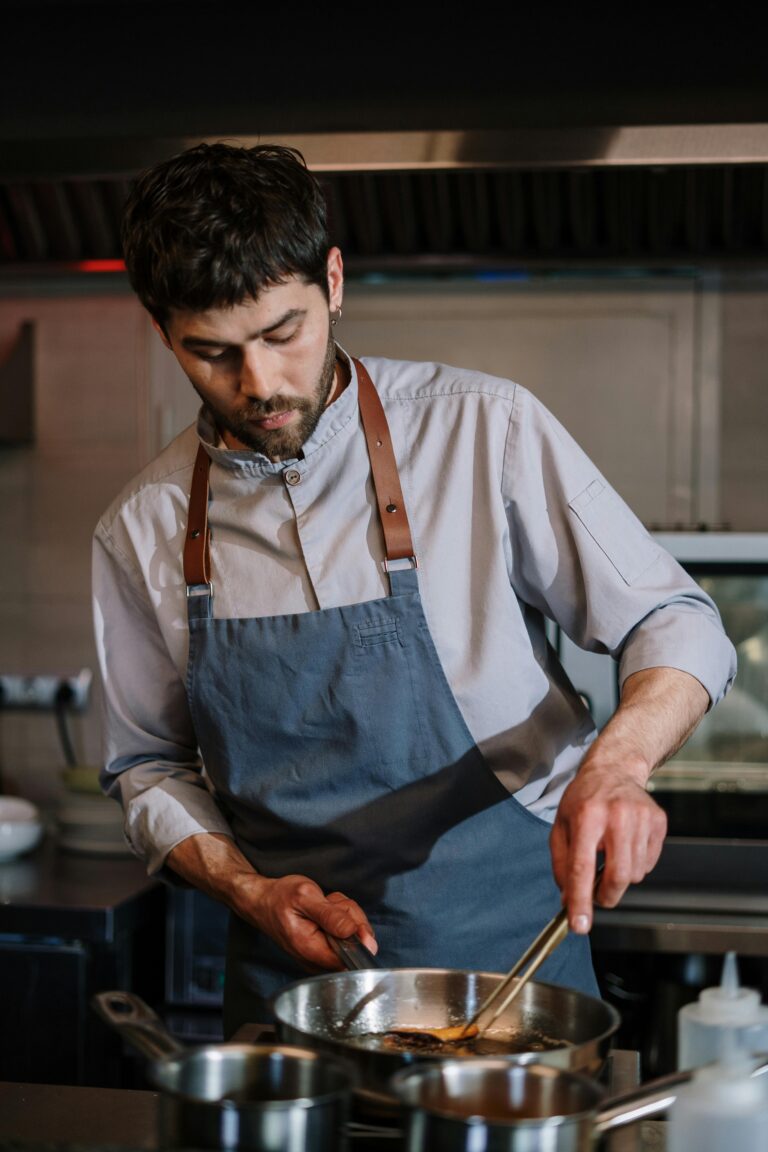 Chef in a blue apron focused on preparing food in a professional kitchen setting.